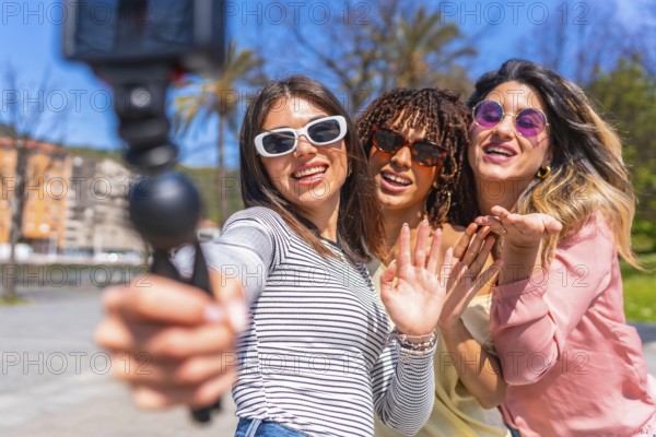 Three cheerful young women enjoying a summer day in the city, capturing a fun selfie with a gimbal, radiating happiness and friendship