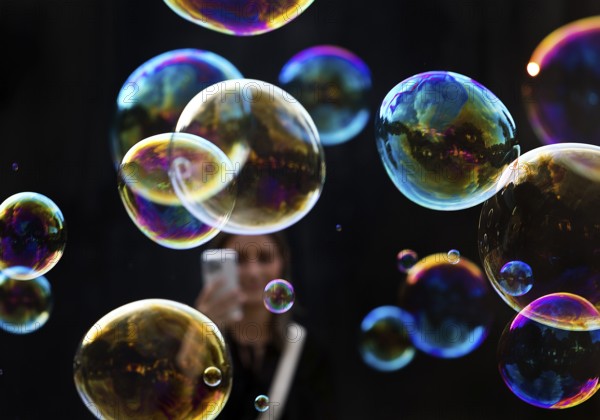 A woman photographs shimmering and floating soap bubbles against a black background, Recklinghausen, North Rhine-Westphalia, Germany