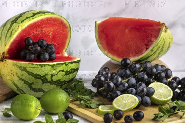 Sliced watermelon, grapes and limes on a wooden board with mint leaves