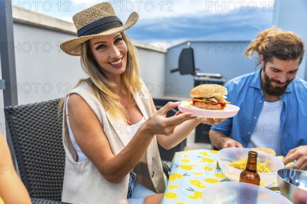 Smiling woman holding a freshly grilled burger during a rooftop barbecue party with friends, enjoying summer vibes and delicious food