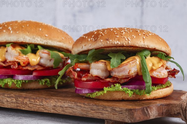 Two shrimp burgers and buns with sesame seeds, bacon, lettuce, tomatoes and onions, On a wooden board