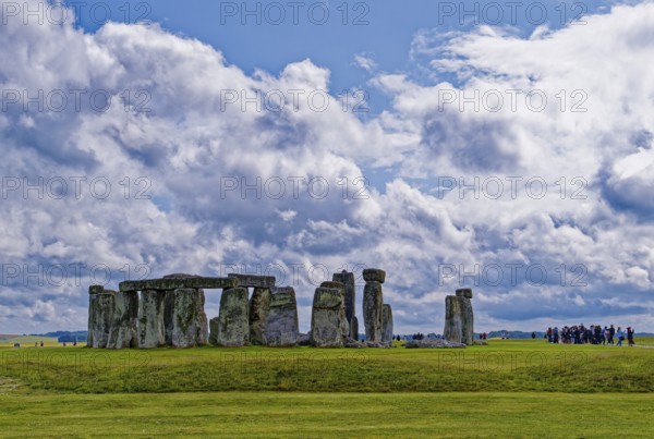 A group of tourists visits Stonehenge. The stone circle, a National Trust, UNESCO World Heritage Site, is a megalithic structure from the Neolithic period and is considered a place of power. The site consists of a ring-shaped earth wall, inside which there are various formations of carved stones grouped around the centre. Amesbury, Wiltshire, South England, Great Britain