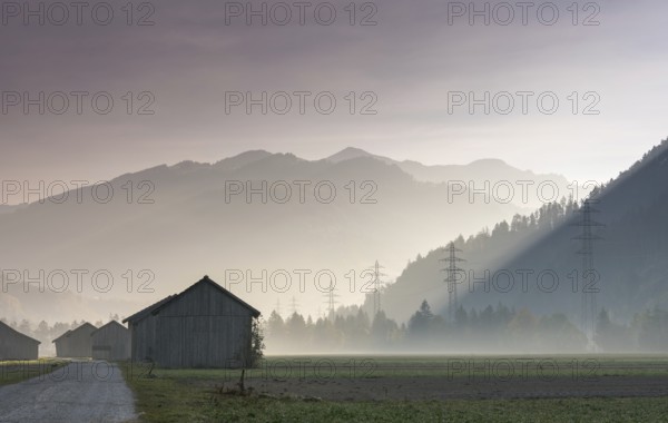 View of the Praettigau Valley near Klosters in Switzerland on an early morning with farm fields and wooden barns and power lines and mountains in silhouette behind in late autumn