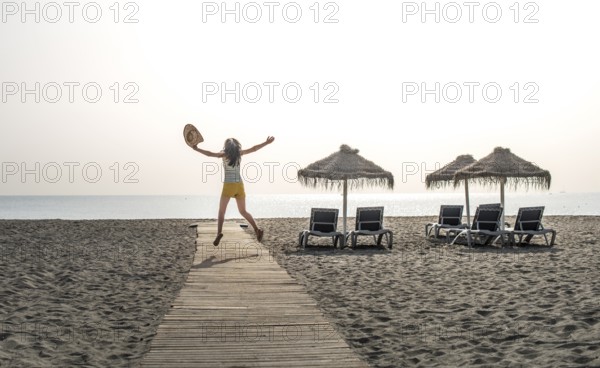 Wooden path to the beach, umbrellas and jumping woman