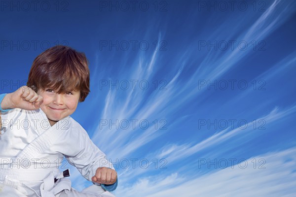Handsome boy in a white kimono practices judo. Background - flying cirrus clouds and blue sky. Concept - photo advertising, children, sports