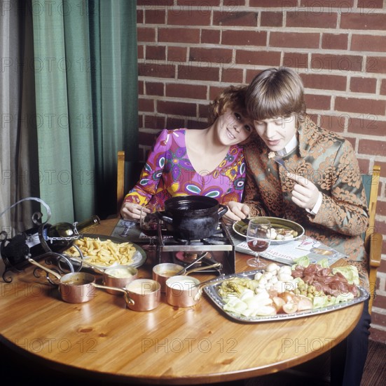 Fondue. A dish that had its breakthrough in the 60s and 70s. A fondue pot with hot oil stands in the middle of the table and you dip meat into it to cook and eat yourself. She is wearing a very colorful and patterned long sleeved blouse that was typical of the late 60's and 70's. Him in a pop inspired jacket not unlike the clothing that singers wore at the time. Sweden 1970. Conard ref CV49-5