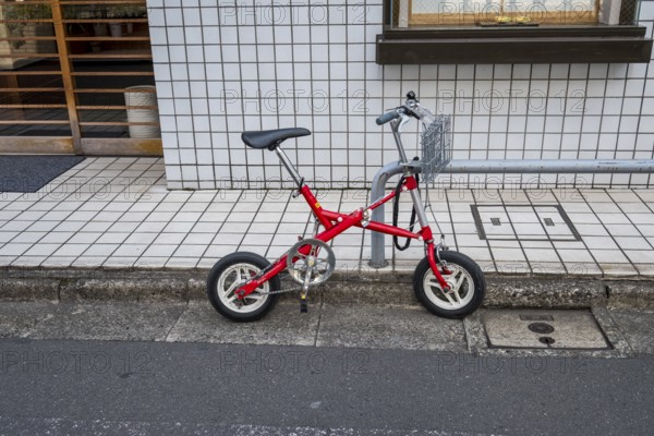 Small red folding bike with basket attached to railing