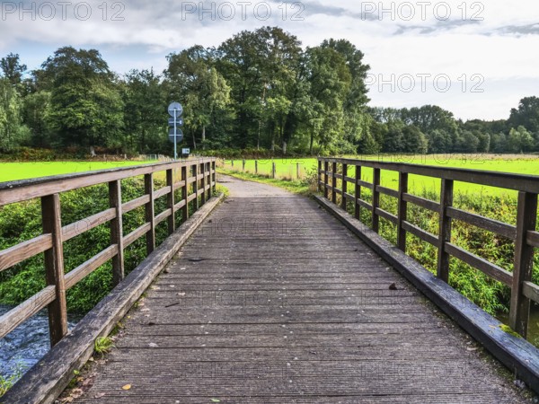 A wooden bridge leads over a river and offers a beautiful view of the surrounding area, vreden, münsterland, germany