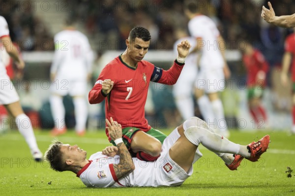 Football match, captain Cristiano RONALDO CR7 Portugal kneeling on the stomach and partly on the abdomen of Kamil PIATKOWSKI Poland with both fists pointing upwards and looking down at his opponent, Kamil PIATKOWSKI Poland lying on the ground on the grass screaming with his legs raised upwards, Estadio do Dragao, Porto, Portugal