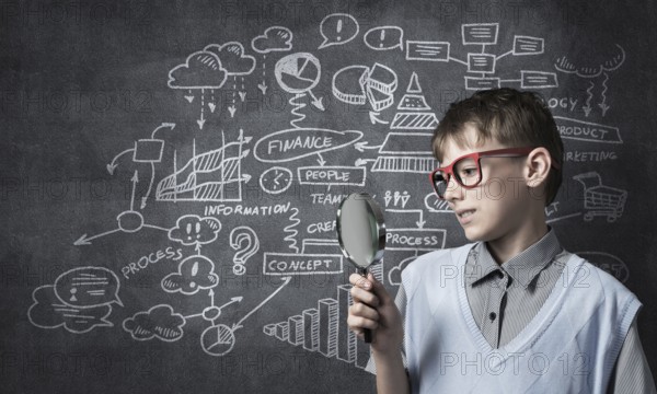 Cute boy looking through magnifying glass against blackboard background