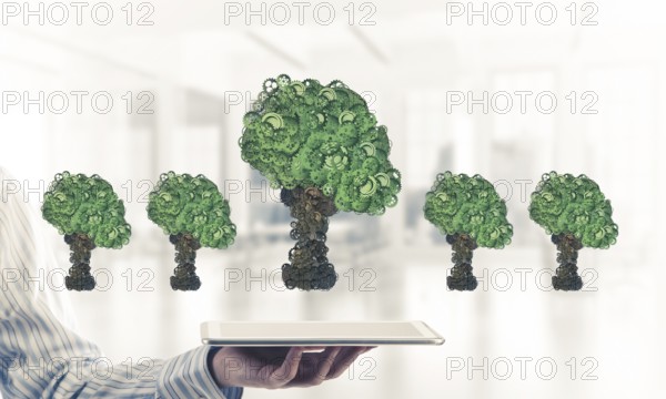 Close of businessman holding tablet pc with green tree made of gears and cogwheels. Mixed media