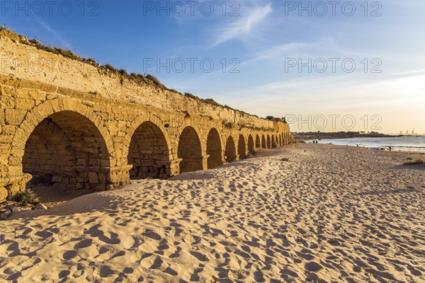 The aqueduct, built in the early Byzantine period. Fantastic sunset on the Mediterranean coast in Caesarea. The sandy beach is trampled by tourists. Concept of active, ecological and historical tourism