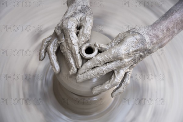 Pottery, artist muddy hands making clay pot giving shape on spinning wheel, semi urban village Dilwara, Udaipur, Rajasthan, India