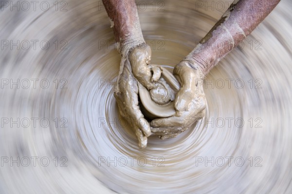 Pottery, artist muddy hands making clay pot giving shape on spinning wheel, semi urban village Dilwara, Udaipur, Rajasthan, India