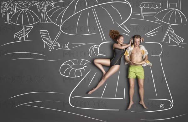 Love story concept of a romantic couple lying on an air mattress against chalk drawings background. Male listening to the music in the headphones and reading a book, female trying to attract his attention