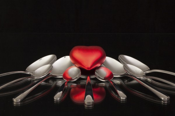 Nine spoons and red heart on a black glass desk