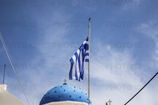 Greek flag waving in the wind, blue church dome, Timios Stavros church, Perissa, Santorini island, Cyclades, Greece