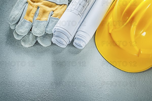 Rolled blueprints hard hat safety gloves on concrete background
