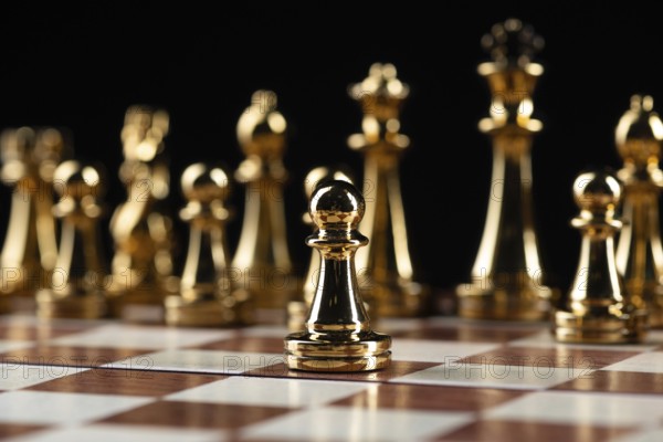 Golden chess figures standing on wooden chessboard. Intellectual duel and tactical battle in business. Strategy planning and leadership concept. Gold metal chess pieces in row on black background