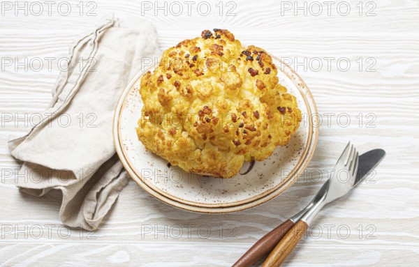 Whole roasted head of cauliflower with olive oil on plate on white wooden rustic table top view with cutlery. Vegetarian dish, food photography, food photography