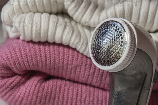 Anti-pilling razor. Device for shaving clothes. Anti-Plush fabric Shaver. Electric portable sweater pill defuzzer Lint remover from pink acrylic or wool sweater. Electric device fabric shaver after cleaning and collected fluff lint. Closeup Pilled sweater. Old used clothes with pilling