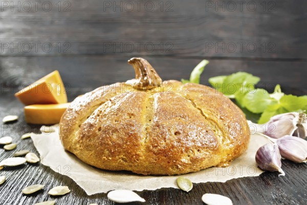 Pumpkin bread on paper, garlic, basil, pieces and seeds of a vegetable on the background of a dark wooden board