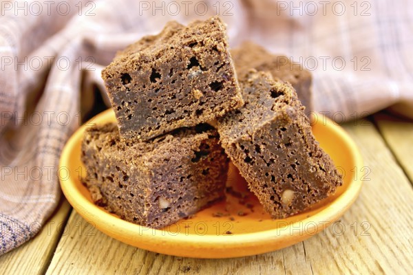 Piece of chocolate cake in a clay plate, napkin on a wooden boards background
