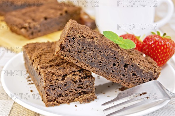 Two pieces of chocolate cake on a plate with strawberries and mint on a fork against a linen tablecloth