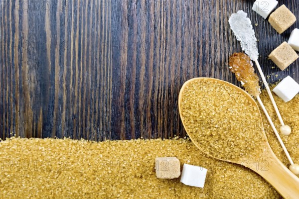 Sugar brown and white granules in a spoon, cubes and crystals on a stick in the form of a frame on the background of a wooden board