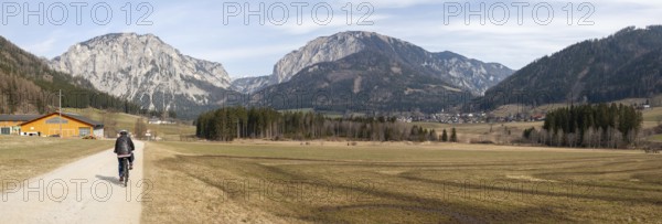 Cyclist on the Lamingtal cycle path between farmland in spring, Pribitz mountain and Meßnerin mountain, in the valley Tragöß Oberort, Hochschwab region, panoramic shot, near Tragöß, Styria, Austria