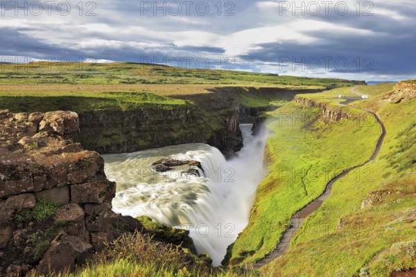 Grand Gullfoss in Iceland. Summer sunny day. Roaring water lit by the morning sun. The river banks are overgrown with green moss northern