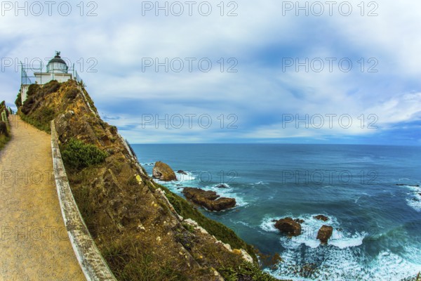 The white building of the lighthouse looks spectacular on a high cape. New Zealand. Nugget Point Lighthouse. Direct path leads to the lighthouse. The concept of active, environmental and photo tourism