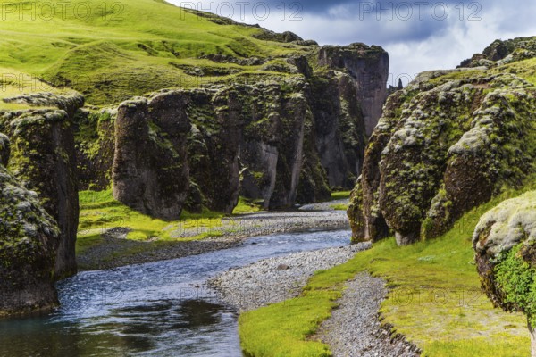 The beginning of the canyon Fyadrarglyufur, Iceland. The sheer cliffs covered with green moss enclose the channel of the brook with melted water. The concept of active, eco and photo tourism
