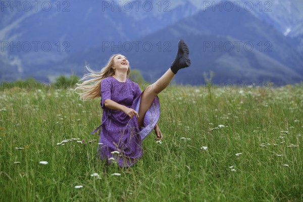 Playful blond woman having fun in the field and raising her leg, USA