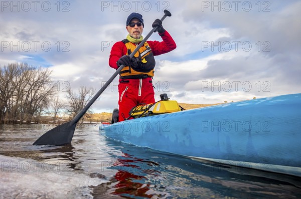 Senior paddler in a dry suit and life jacket is training on stand up paddleboard on a mountain lake in winter conditions - Horsetooth Reservoir in northern Colorado, POV from an action camera