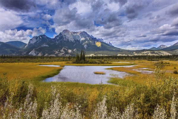 Cloudy Indian summer in the Rockies of Canada. Rocks, lakes and yellow grass under flying clouds. Concept of active automobile and ecological tourism