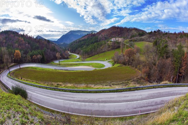 Wet asphalt. Cloudy winter day. The picturesque mountain slopes are covered with coniferous forest. Winding mountain road serpentine after the rain. Magnificent Umbria in December