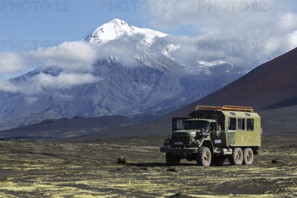 TOLBACHIK VOLCANO, KAMCHATKA, RUSSIA, AUG 27, 2014: Russian off-road extreme expedition truck ZIL-131 (6-wheel drive) on mountain road on volcanic slag field on background of beautiful volcano. Russia, Kamchatka, Klyuchevskaya Group of Volcanoes