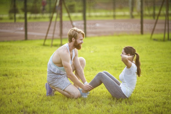 Sit ups fitness couple exercising sit up outside in graß Fit people working out cross training. Woman doing abdominal crunches press exercise with trainer. Couple Doing Sit-Ups Abdominal Crunch