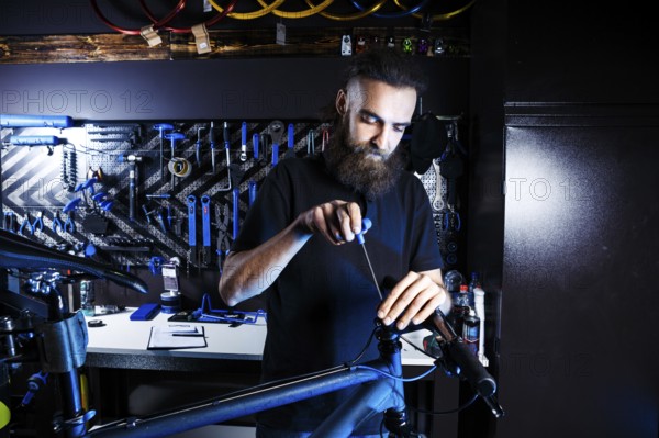Theme sale and repair of bicycles. Young and stylish with a beard and long hair, a Caucasian man uses a tool to set up and repair a bike in a store. Business owner at work