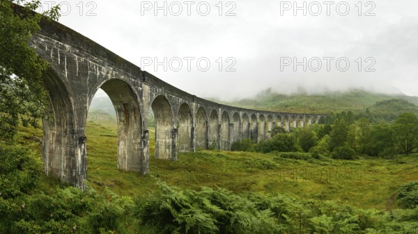 High resolution panorama of Glenfinnan railway viaduct (location from Harry Potter movie) shot from side, on overcast day with grey sky and lot of green grass and trees around. Inverness, Scotland, United Kingdom