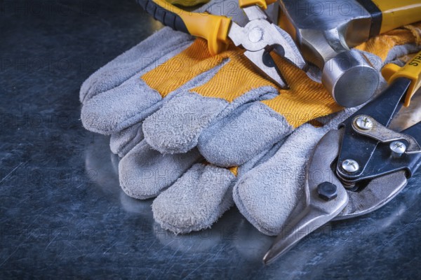 Protective gloves with claw hammer pliers and tin snips on scratched vintage metallic background construction concept