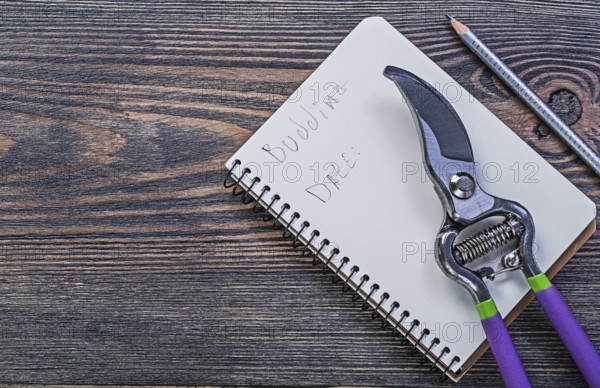 Notepad pencil secateurs on vintage wooden board gardening concept