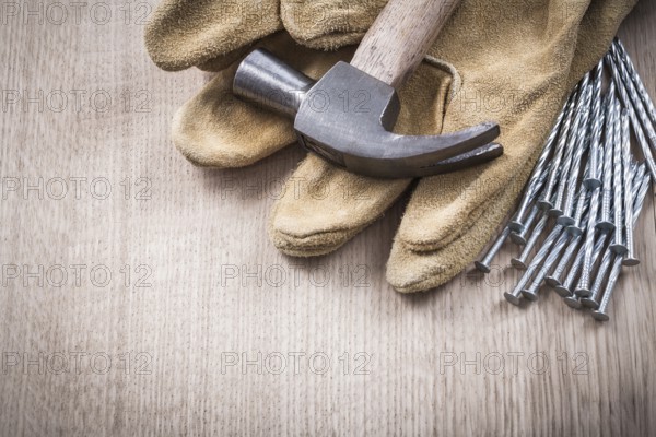 Claw hammer leather protective gloves and heap of metal nails on wooden board close up version construction concept
