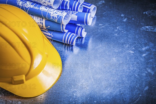 Blue construction drawings yellow hard hat on scratched metallic background