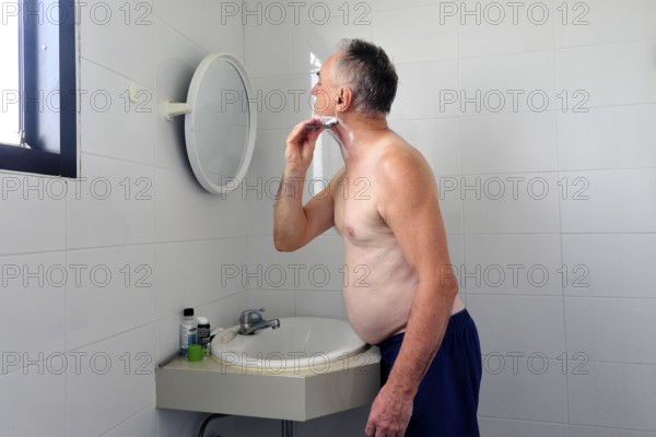 Man 60 plus shaves wet in the bathroom