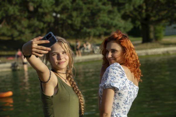Two close friends take a joyful selfie by a serene and beautiful lake, capturing the essence of summertime vibes