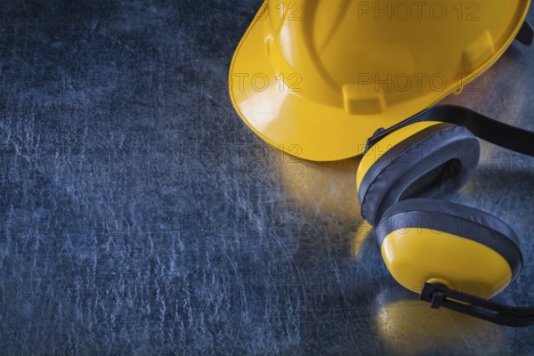 Noise insulation ear muffs and hard hat on scratched metallic background copy space image construction concept