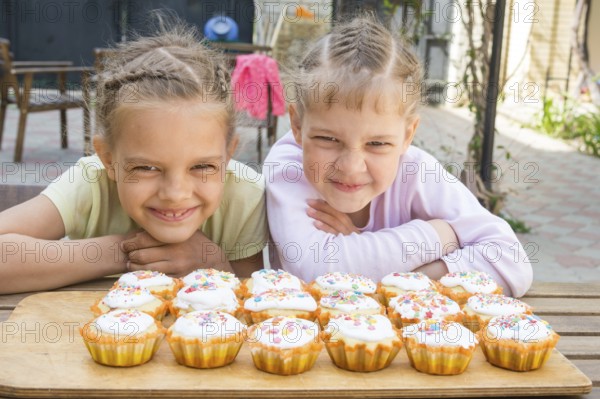 Two girls pretending funny faces, sitting in front of easter cupcakes