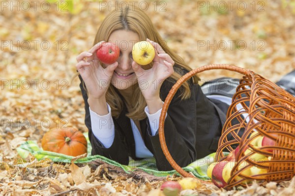 Young beautiful girl lying on the leaves in the autumn forest in the fun and put the apples to the eyes